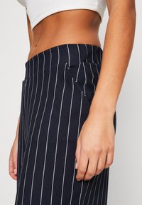 Mörkblå randiga byxor med mjuk textur, elastisk midja och sidofickor. Nära bild betonar tyg- och mönsterdetaljer.