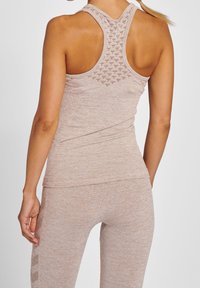 Vaaleanruskea urheilullinen tank top, jossa on teksturoitu selkädesign ja kisavälikohta, yhdistettynä samanvärisiin vaaleanruskeisiin legginsseihin. Silkkinen kangas.