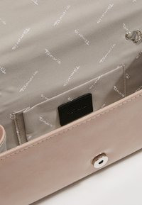 Beige kabelka uvnitř s několika kapsami, textilní podšívka potištěná logem "Tamaris" a kovové západkové zavírání na vnějším okraji.