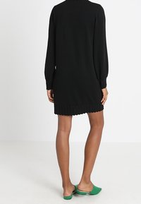 Robe en tricot noir à manches longues, ourlet côtelé et coupe ample, associée à des chaussures vertes à enfiler.