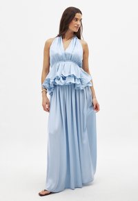 Robe maxi bleu clair avec un col halter, un buste à volants et une jupe fluide. Fabriquée à partir d'un tissu doux, elle présente des détails froncés.