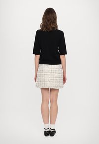 Top negro de manga corta combinado con una minifalda blanca texturizada. Calzado negro con tachuelas plateadas. Vista trasera sobre un fondo liso.