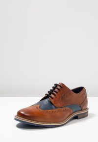 Scarpa in pelle marrone con lacci, pannello texturizzato blu navy, dettagli brogue, punta arrotondata e suola beige. Design classico con colori a contrasto.