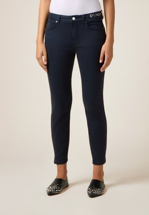 Dunkelblaues Slim-Fit-Jeans aus Denim mit funktionalen Taschen und einem Gürtel, der eine dekorative metallische Akzentuierung aufweist.