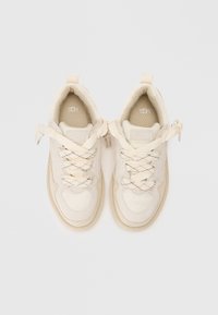 Sneakers beige chiaro realizzati in rete e camoscio, con punta rotonda, accenti texturizzati e lacci decorativi, con un piccolo logo sulla linguetta.