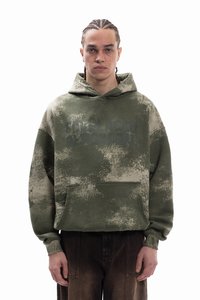 Zelená, volná mikina s kapucí s texturovaným vzorem batiky a přední kapsou. Na hrudi má jemný grafický potisk.