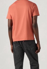 T-shirt texturé corail à manches courtes, associé à un jean en denim gris foncé avec des coutures sur les poches arrière.