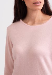 Jasnoróżowy, miękki sweter z dzianiny z okrągłym dekoltem i długimi rękawami, charakteryzujący się gładką fakturą i minimalistycznym wzornictwem.