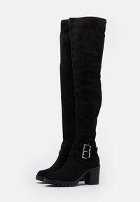 Botas de ante negras hasta la rodilla con un tacón grueso, acentos de dobles hebillas y un acabado texturizado, que cuentan con cremalleras laterales para facilitar su uso.