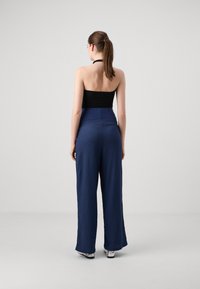 Haut noir à encolure dégagée associé à un pantalon large en tissu texturé bleu marine. Le pantalon a une taille haute et une coupe fluide et décontractée.