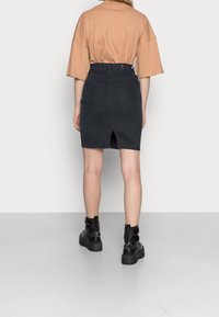 Falda de mezclilla negra con apertura en la parte trasera, dos bolsillos traseros, combinada con una camiseta oversized beige y botines de plataforma negros.