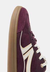 Baskets en daim violet avec lacets blancs, logo latéral blanc et semelle épaisse en caoutchouc marron, vues de côté en gros plan.