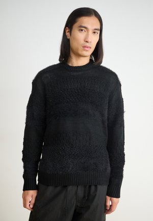 Black knitted sweater featuring textured patterns, varying weaves, and a ribbed neckline. Long sleeves with a relaxed fit.