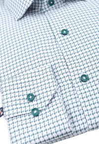 Gestrikte blouse in het wit met een teal geometrisch patroon. Heeft een spread collar en contrasterende teal knopen. Zachte stofstructuur.