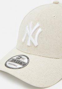Casquette beige ajustable avec un logo brodé blanc des New York Yankees, un tissu texturé et une étiquette circulaire New Era 9FORTY.