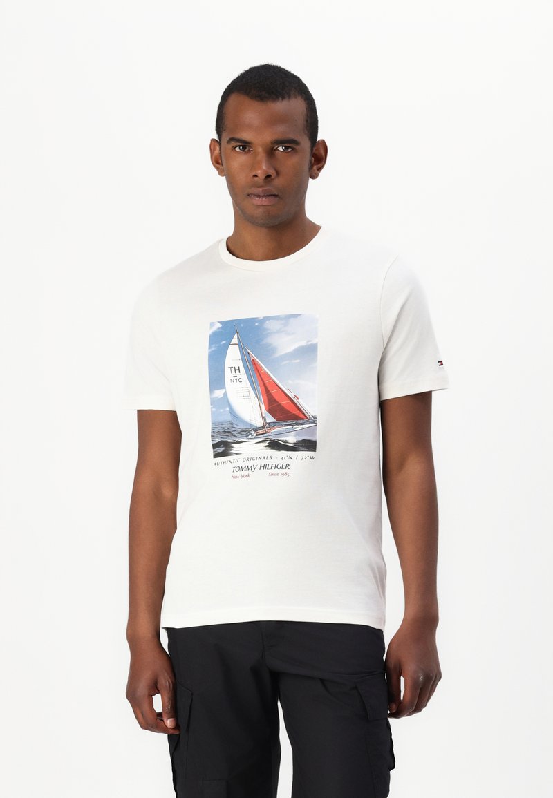 Camiseta de algodón blanca con un gráfico de un velero con velas rojas y azules. Mangas cortas, escote redondo y detalle del logo en la manga.