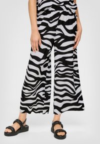 Pantalons larges à motifs zèbre noir et blanc avec un tissu texturé et une taille élastique, associés à des sandales noires chunky.