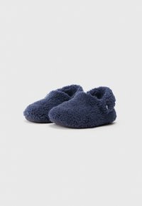 Par de zapatillas azul marino de felpa, tipo slip-on, con un exterior suave y texturizado y un bajo soporte para el talón sobre un fondo blanco.