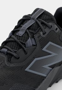 Schwarze Sportschuhe mit einem Obermaterial aus Mesh, Gummisohle, prominenten grauen Logo an der Seite und detaillierter Schnürung. Texturierte Einsätze überall.