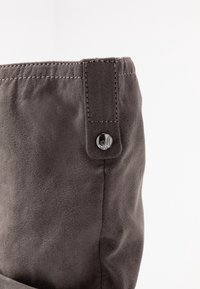 Haut de botte en daim gris avec un bord cousu et un détail de bouton sur une boucle de ceinture. La texture est douce avec une finition lisse.