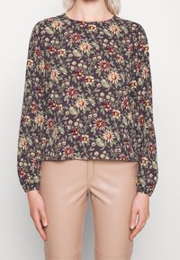 Haut à manches longues florales en tissu gris foncé, présentant une variété de fleurs en crème, rose et vert. Coupe ample avec poignets élastiqués.