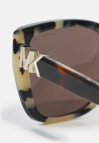 Ochelari de soare tortoiseshell cu lentile maro închise, având un design unghiular modern și accente din metal aurit la balamale.