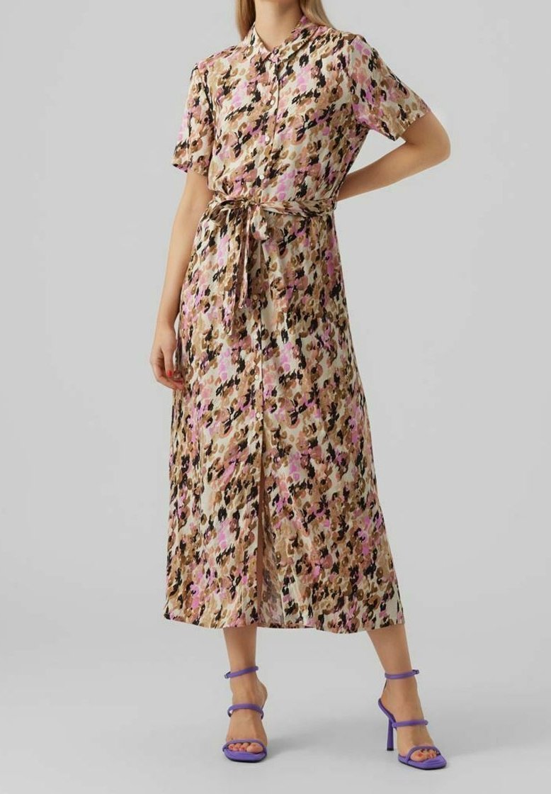 Maxi šaty s vzorem v béžové barvě s růžovými a černými akcenty, krátkými rukávy, knoflíkovým zapínáním vpředu a páskem v oblasti pasu. Nosené s fialovými sandály na vyšším podpatku.