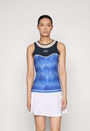 Canottiera atletica con gradiente blu e bordi in blu scuro, scollo rotondo, dettaglio del logo e design aderente, abbinata a una gonna plissettata bianca.