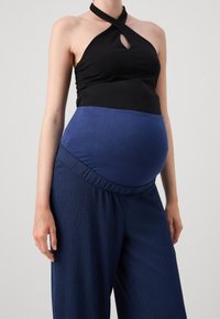 Zwarte haltertop met een keyhole-detail, gecombineerd met stretchy donkerblauwe broek met een geraffineerde tailleband, ontworpen voor zwangerschapskleding.