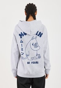 Šedá mikina s kapucí, na zadní straně s modrou kreslenou postavičkou a textem "Moomin" a "80 let" níže. Měkká tkanina, volný střih.
