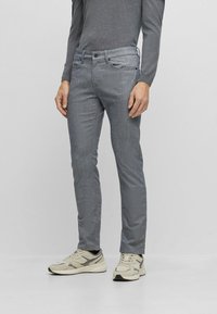 Pantalon gris ajusté en matière douce, avec des poches latérales, une fermeture à bouton et à glissière, et une texture subtile.