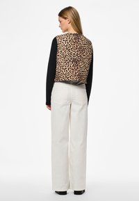Skraćeni prsluk od tkanine s leopard printom i okruglim izrezom, uparen s bijelim hlačama širokih nogavica visokog struka i crnim platformama.