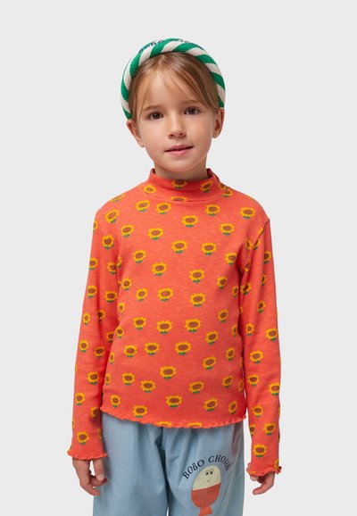 Top de cuello alto acanalado naranja con un estampado repetido de girasoles en amarillo y tallos verdes. Con dobladillo ajustado y mangas largas.