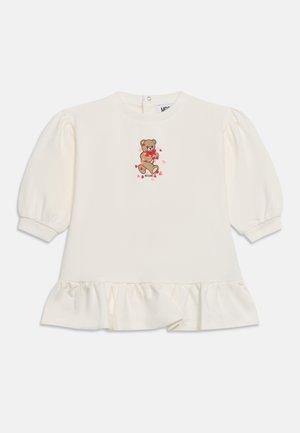 T-shirt bébé à manches longues couleur crème avec ourlet à volants et manches bouffantes, avec un ours en peluche tenant des cœurs rouges sur la poitrine.