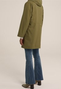Olive green hooded raincoat with a straight cut, adjustable cuffs, and a mid-length design, paired with flared blue jeans and brown ankle boots.