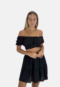 Zwarte off-shoulder crop top en gelaagde rok in lichtgewicht stof, met gerimpelde accenten en een vloeiend ontwerp.