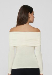 Off-Shoulder Langarm-Oberteil in hellem Creme, mit gerafftem Ausschnitt und taillierter Silhouette, aus einem weichen Stretchstoff gefertigt.