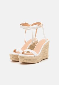 Sandales blanches à talon wedged avec une semelle texturée de style espadrille, dotées de deux fines brides et d'une bride de cheville avec une boucle décorative.