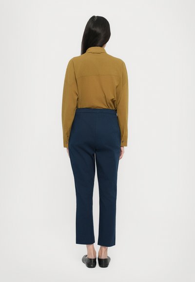 Svetlo rjavo dolgo-sleeve srajco z gumbi na zapestjih in temno mornarsko ozke hlače z gladko teksturo in dolžino do gležnjev. Črne balerinke.