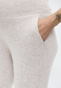 Χέρι με τατουάζ ήλιου και ημισελήνου που ακουμπάει μέσα στην τσέπη μπεζ π λεκτού παντελονιού με κηλίδες.