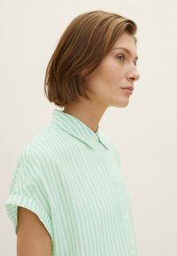 Kurzarmhemd in Hellgrün mit weißen vertikalen Streifen, ausgestattet mit einem Kragen und einer glatten Stofftextur.