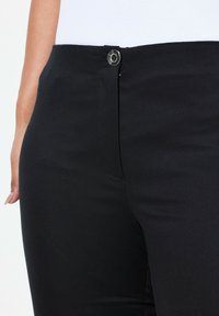 Schwarze Hose mit glatter Textur, ausgestattet mit einem vorderen Knopfverschluss und schlanker Passform. Das Design umfasst ein dezentes Taschen-Detail.