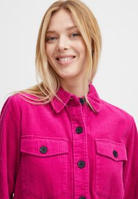 Fuchsia Cord-Jacke mit kragenförmigem Ausschnitt, zwei Brusttaschen und schwarzen Knöpfen, die eine strukturierte Ripp-Optik und ein lässiges Design präsentieren.