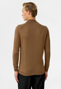 Bruine gebreide trui met lange mouwen, een ronde hals en geribde manchetten. Heeft een gladde textuur en naden bij de schouders.