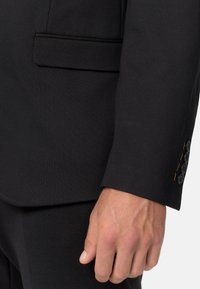 Rukav crnog odijela s glatkom teksturom, elegantnim dizajnom i naglaskom na manžetnu s tri dugmeta. Suptilan detalj džepa je vidljiv.
