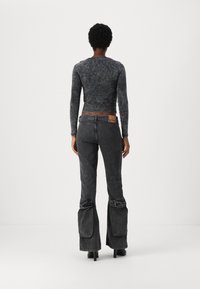 Top noir à manches longues, court, associé à un jean gris taille haute évasé avec un look usé et des accents froncés au niveau des chevilles.