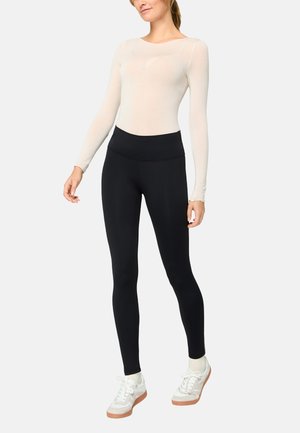 Woman wearing a fitted long-sleeve beige top, high-waisted black leggings, and white sneakers with light brown soles.