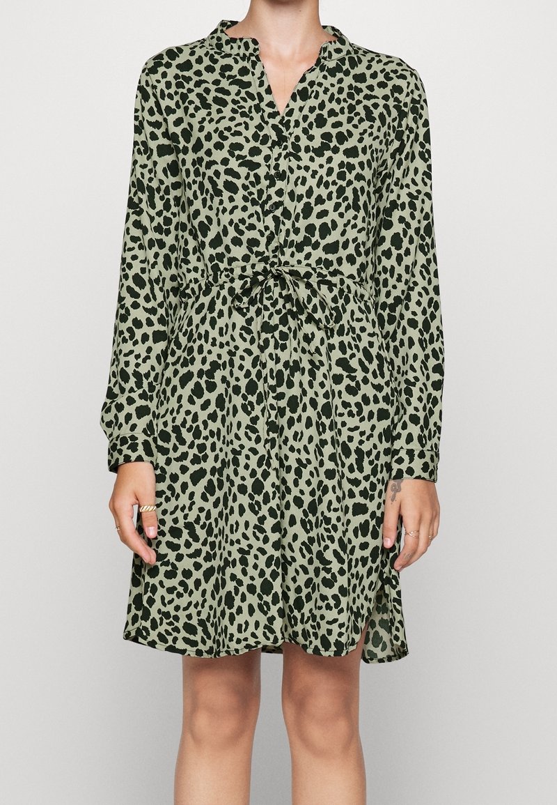 Grøn leopardprint kjole med krave, knaplukning foran og lange ærmer; bæltestrop i taljen og sideskår for nem bevægelse.