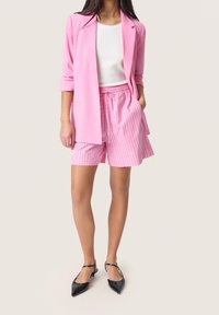 Blazer rosa y pantalones cortos a rayas rosa claro con cintura elástica; blusa blanca de canalé debajo; tacones negros de punta.