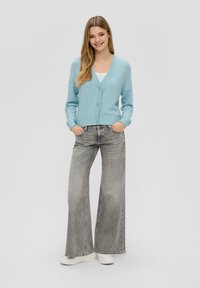 Jasnoniebieski sweter z dzianiny z dekoltem w serek, zapinany na guziki, z prążkowanymi mankietami, w połączeniu z szarymi spodniami o szerokich nogawkach i białymi trampkami.
